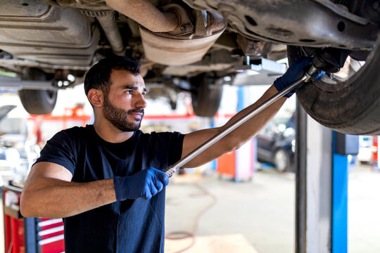 Focused male mechanic with metal wrench screwing detail of car wheel while working in service