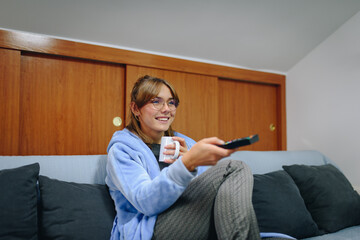 Girl sitting on a sofa in a robe and using a remote control television