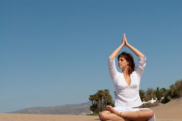 woman dressed in white performing meditation and yoga postures on the sand dunes on sunny day