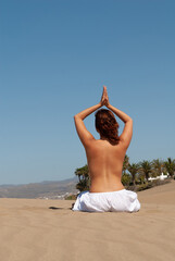 Fototapeta na wymiar woman dressed in white performing meditation and yoga postures on the sand dunes on sunny day