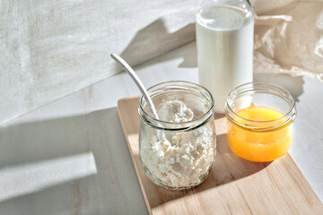 Homemade Natural cottage cheese, fresh curd,  milk, honey in glass jars on light background. Healthy breakfast in a minimalistic style. Dairy. Selective focus
