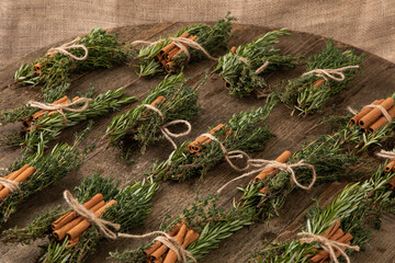 bundles with herbs and cinnamon sticks tied together with a bow on wooden table 