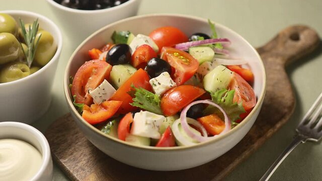 The girl puts a plate with Greek salad on the table, serving with olives, sauce, wooden board