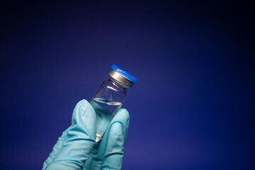 Development of coronavirus vaccine COVID-19. bottle phial with no label in blue medical glove. isolated on blue background. cure. Vaccination for prevention and treatment to infections