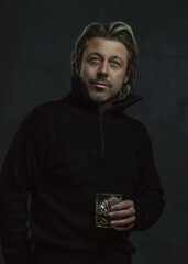 Blonde man in black woolen sweater holding glass of whiskey.