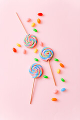 Colorful lollipops swirls on sticks and jelly beans. Striped spiral multicolored candy on pink background, top view