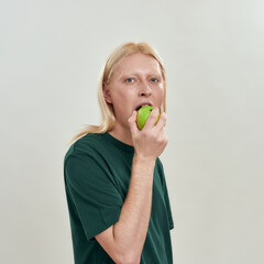 Sensual young caucasian man biting green juicy apple