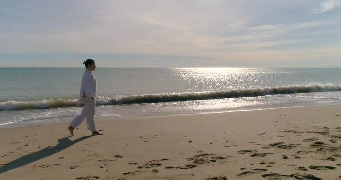 mujer madura de blanco y pelo recogido paseando por la orilla de la playa