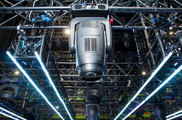 Moving head spotlight device is clamped on a rigging steel truss for lifting. Installation of professional stage light equipment for a concert. - obrazy, fototapety, plakaty