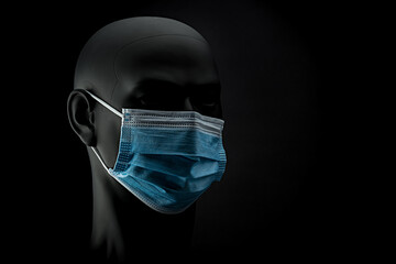 Eine blaue medizinische Mund-Nasen-Maske an einem dunklem Kunstkopf vor schwarzem Hintergrund