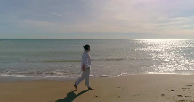 Mujer median aedad paseando por la playa escuchando m&uacute;sica en aud&iacute;fonos
