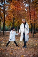 Fototapeta premium Mom and her little daughter in white raincoats hold hands and laugh. Autumn Park. Family day.