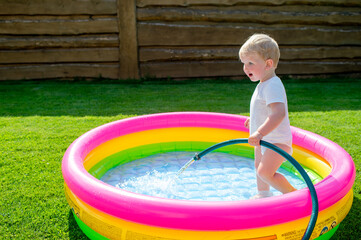A little funny boy collecting water in the children's swimming pool