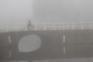 People cycling or waking outdoors during a very foggy, misty day