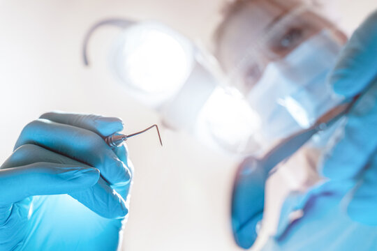 Zahnarzt / Zahn&auml;rztin mit Sonde und OP Leuchte aus Sicht des Patienten dicht &uuml;ber dem Mund bei der Untersuchung mit Corona Maske
