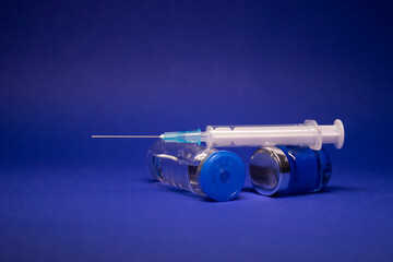 two transparent Vaccine bottle phial with no label, medical syringe injection needle. isolated on blue background. Development of coronavirus vaccine COVID-19. cure. World race in researching