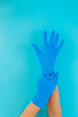 Two hands on a blue background putting on blue latex gloves