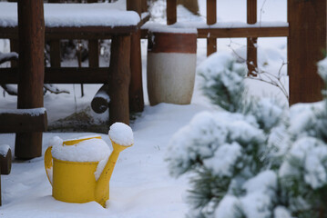 Fototapeta na wymiar yellow watering can in the garden pergola covered with snow 