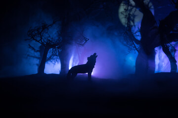Silhouette of howling wolf against dead forest skyline and full moon. Creative artwork decoration.