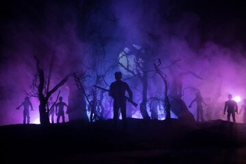 Fototapeta premium Man with riffle against zombie attack. Zombie apocalypse. Scary view of blurred zombies at cemetery and spooky cloudy sky with fog. Horror Halloween concept.