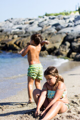 children playing in the sand, on the seashore next to the rocks