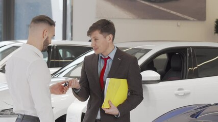 Cheerful car dealer shaking hands with a customer after giving him car keys. Mature salesman congratulating young man with buying new automobile. Car dealership concept