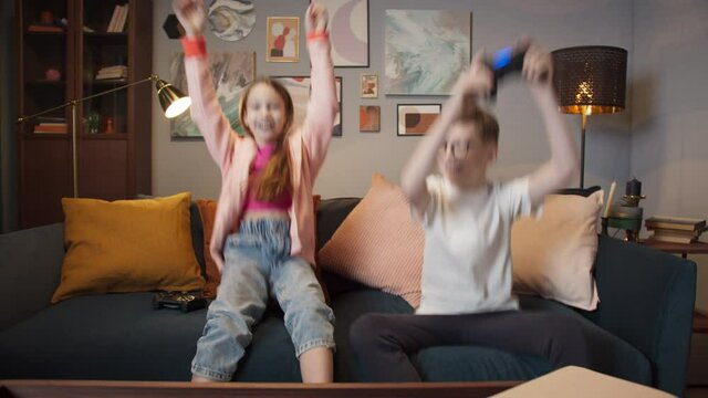 Pretty little girl and boy are playing game console and laughing while sitting on sofa at home, next gen new generation games, happy friend after school, brother and sister