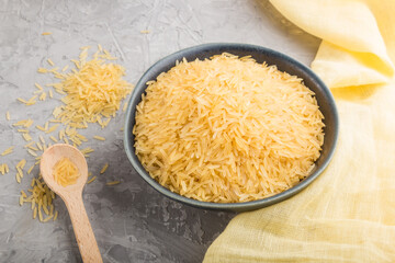 Blue ceramic bowl with raw golden rice and wooden spoon on a gray concrete background. Side view.