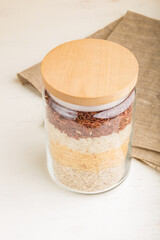 glass jar with different kinds of rice poured in layers on white background. side view, close up.