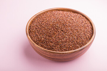 Wooden bowl with raw red quinoa seeds on a pastel pink background.  Side view.