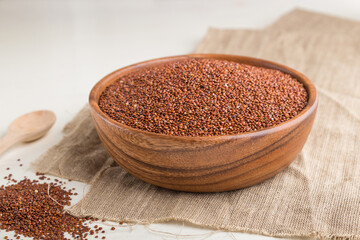 Wooden bowl with raw red quinoa seeds on a white wooden background. Side view, close up, selective focus.