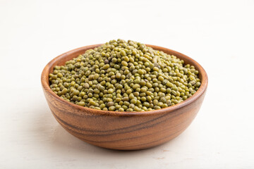 Wooden bowl with raw green mung bean on a white wooden background. Side view.