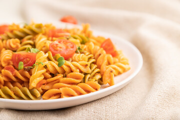 Tortiglioni semolina pasta with tomato and microgreen sprouts on a white wooden background. Side view, selective focus.