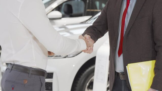 Cropped shot of a man receiving car keys from salesman and shaking hands. Male customer closing the deal of buying new automobile, shaking hands with car dealer