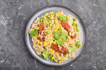Quinoa porridge with green pea, corn and dried tomatoes on ceramic plate on a gray concrete background. Top view.