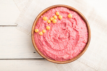 Hummus with beet in wooden bowl on a white wooden background. Top view, close up.