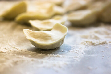 Lots of uncooked dumplings on the surface of a wooden white kitchen table. The process of cooking dumplings, dumplings, ravioli and dumplings. Scattered white flour.