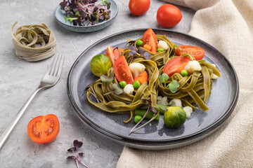 Tagliatelle green spinach pasta with tomato, pea and microgreen sprouts on a gray concrete background. Side view.