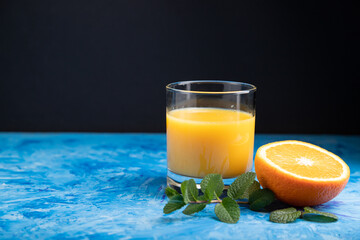 Glass of orange juice with mint on a black and blue background. Side view, copy space.