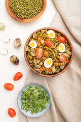 Mung bean porridge with quail eggs, tomatoes and microgreen sprouts on a white wooden background. Top view, close up.