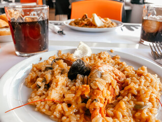 On the table in the restaurant there is a Spanish dish of paella cooked with shrimps and mussels. Restaurant menu or articles on Spanish food..