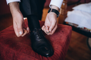 Man tying the laces on black shoes on a wooden floor