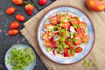 Vegetarian fruits and vegetables salad of strawberry, kiwi, tomatoes, microgreen sprouts on black concrete background. Top view, close up.