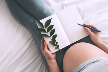 Pregnant woman with beautiful belly makes notes or check list in paper diary. Concepts of...