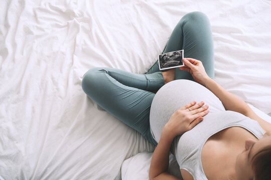 Pregnant woman looking at ultrasound image. Expectant mother with pregnant belly waiting for baby.