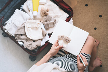 Pregnant woman packing hospital bag with checklist. Expectant mother with travel suitcase of baby clothes preparing for newborn birth, making notes in diary.