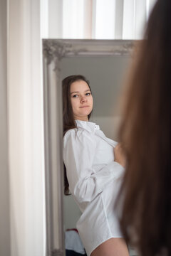 Brunette in mens shirt. Rear view of young woman looking through the mirrow in the morning