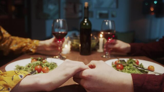 Romantic couple holding hands together during happy saint valentine day dinner, man and woman, lovers at home drinking wine