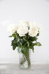 Bouquet of white roses in a glass vase on a beige table against a gray wall. Copy space.