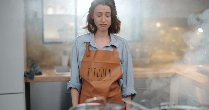 Tired and sad housewife standing hopelessly in a smoky kitchen from burnt food. Exhaustion from household chores and home routine concept